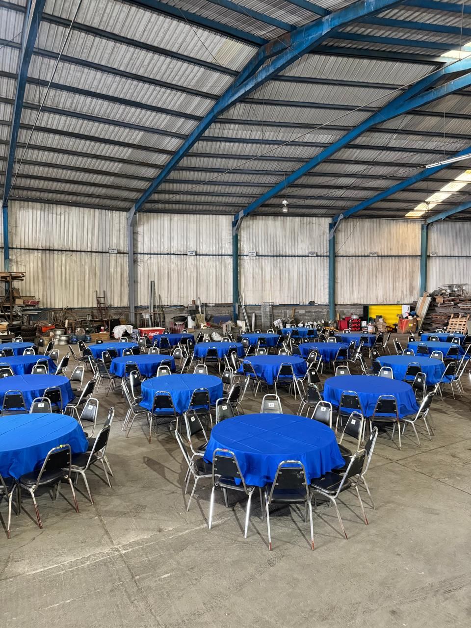 Mesas redondas con mantel azul montadas en nave industrial